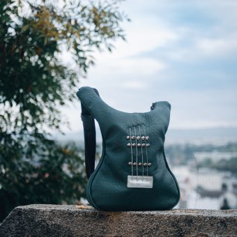 Dark green Italian leather guitar-shaped bag with authentic guitar strings, perfect for fashion-forward music enthusiasts.