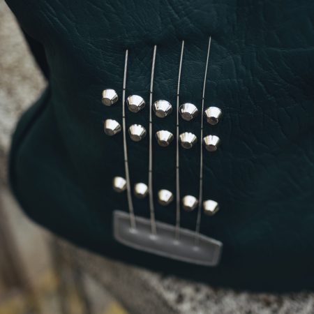 Dark green Italian leather guitar-shaped bag with authentic guitar strings, perfect for fashion-forward music enthusiasts.